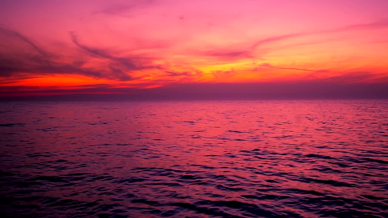 美丽的涟漪海浪与反射粉红色的夕阳光在紫色和黄色的天空背景。平静的海浪场景，与云的海滩，慢动作，平移，高清。ProRes 422 HQ。视频素材