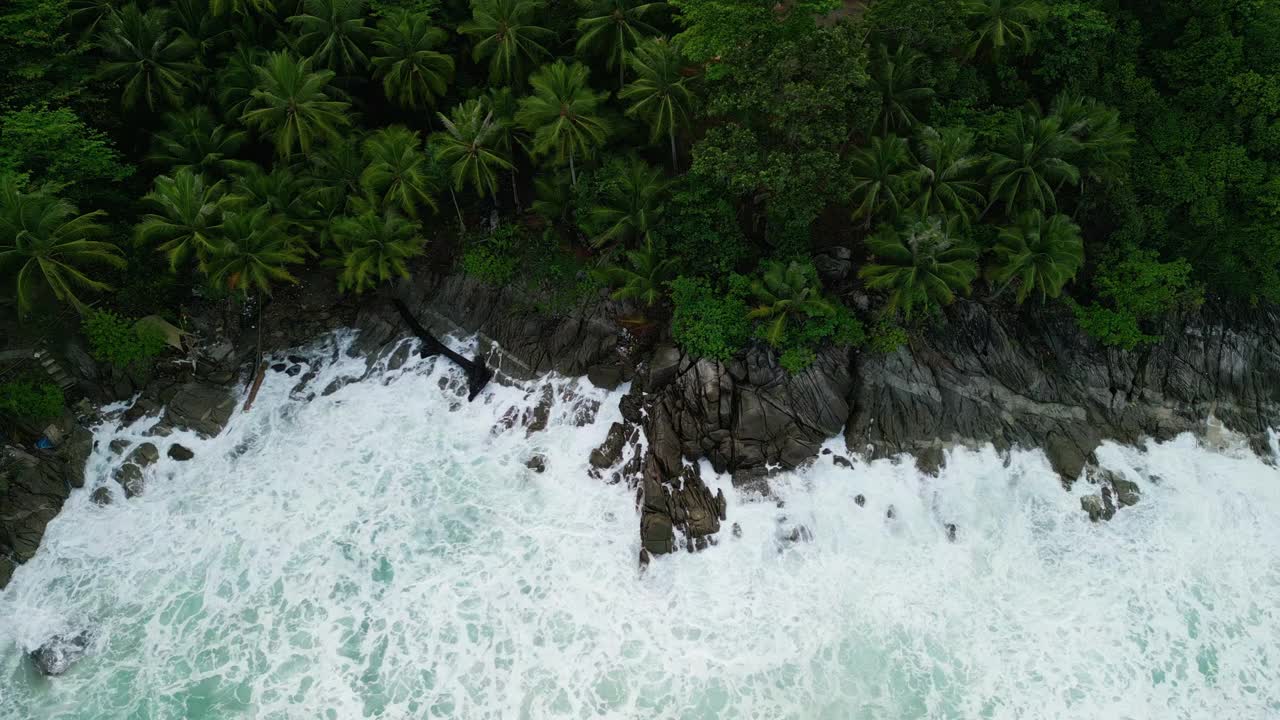 海滩鸟瞰图椰子树和巨大的海浪造成的强风造成的巨浪冲刷在泰国普吉岛海岸线上的山丘。视频素材