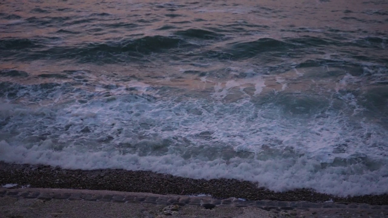 在日落黄昏的海滩上，海浪冲击沙滩的特写。黄昏的海洋潮汐溅起海岸线。特写白色泡沫水面风暴视频素材