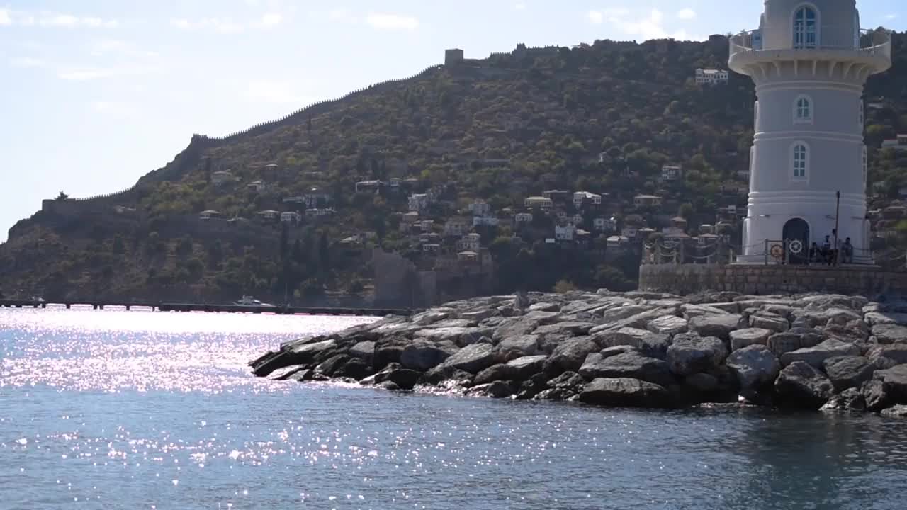 在海上，一艘旅游船上的运动经过阿拉尼亚灯塔，背景是海岸线和山上的老城。视频12秒视频下载