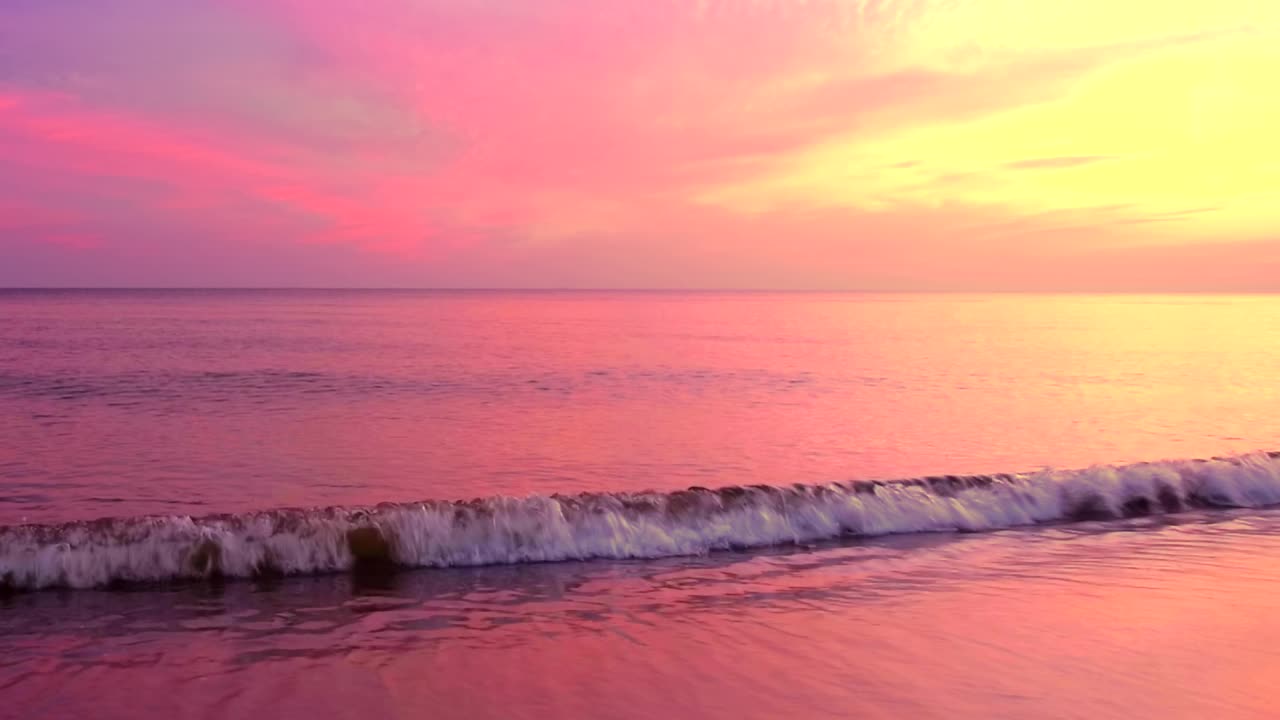 美丽的波纹海岸与反射粉红色的日出光在紫色和黄色的天空背景。风平浪静的场景，海边的云，慢动作，高清。ProRes 422 HQ。视频素材