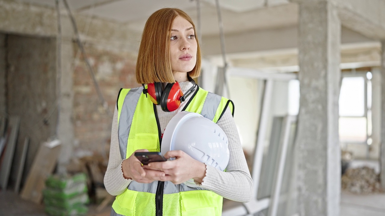 年轻的金发女建筑师在建筑工地用智能手机戴着安全帽视频素材