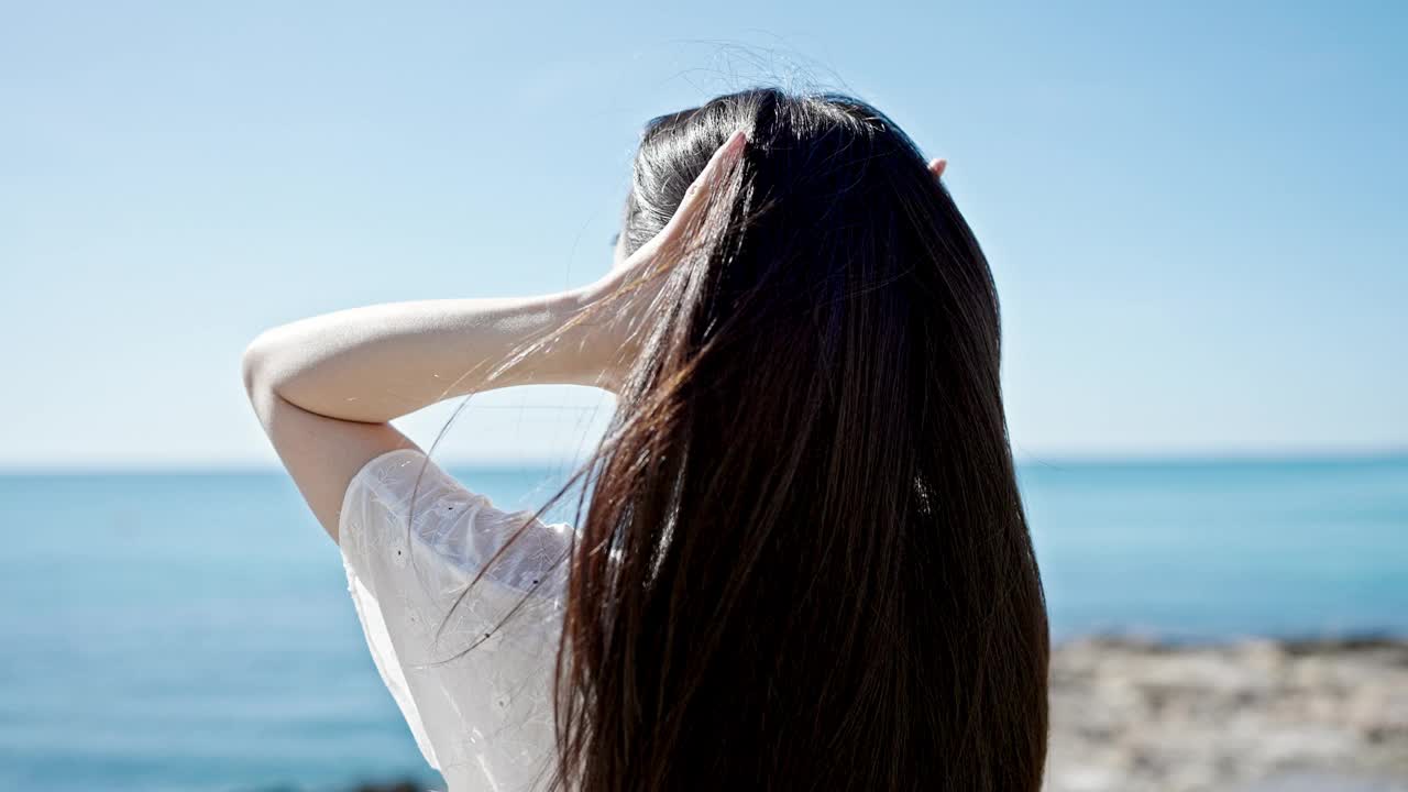 年轻的中国女游客微笑着自信地在海边用手梳头视频素材