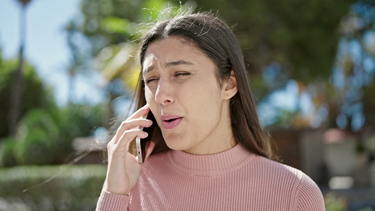 年轻漂亮的西班牙女子在公园用智能手机说话，表情严肃视频素材