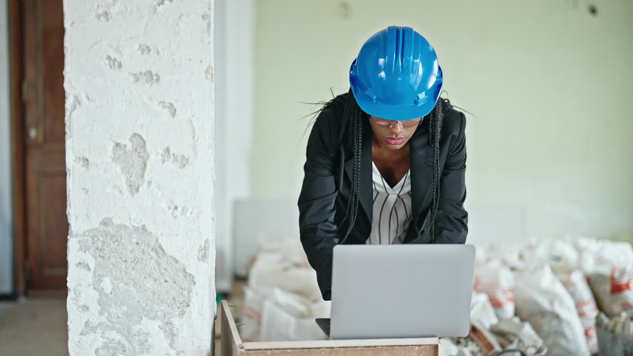 非裔美国女建筑师在工地用笔记本电脑取下眼镜和安全帽视频素材