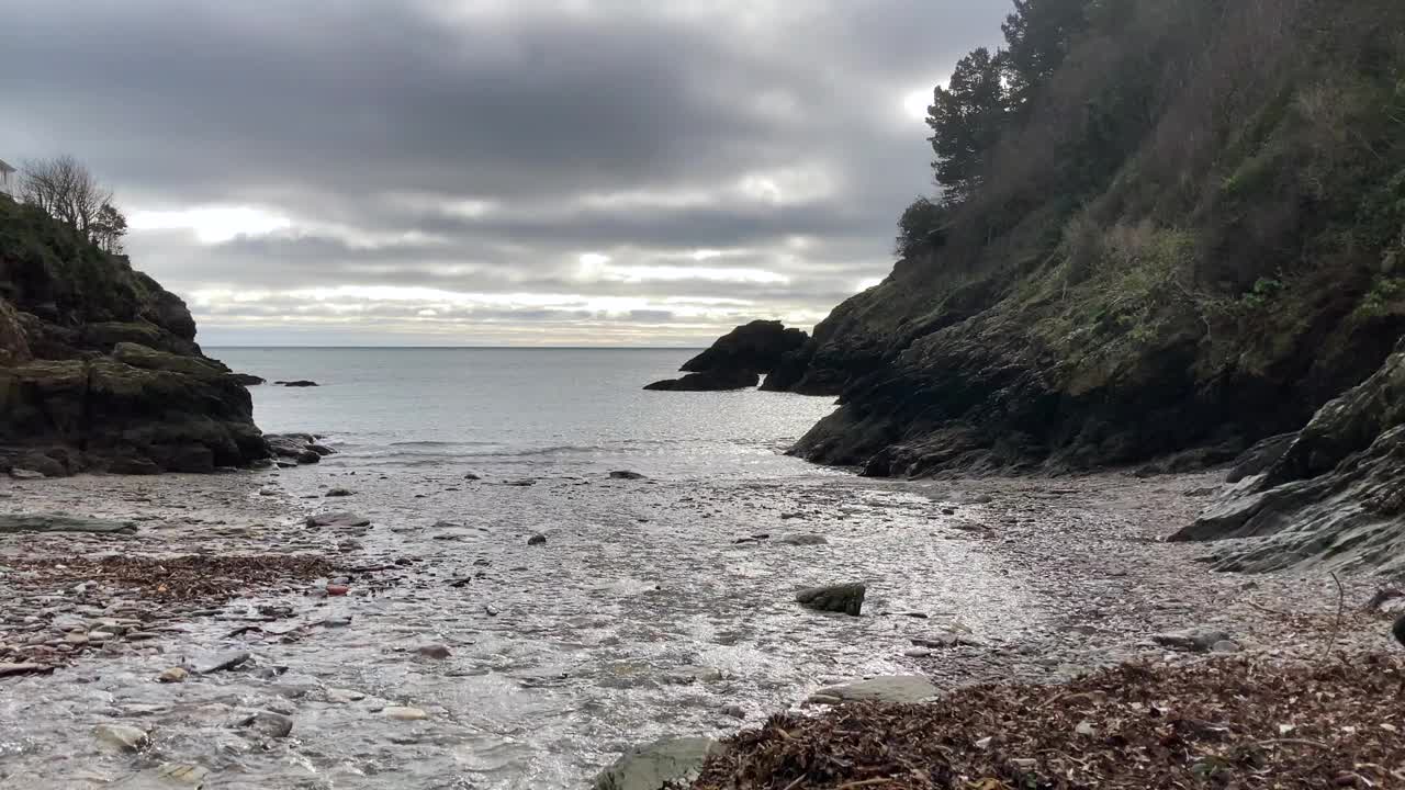 在英国德文郡，一名妇女和她的黑色拉布拉多犬在悬崖环绕的海滩上散步视频素材