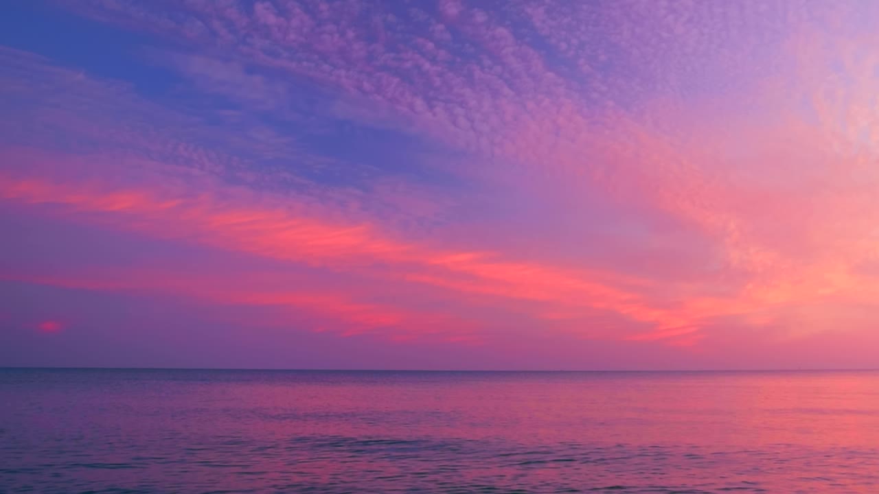 美丽的涟漪海浪与反射粉红色的日出光在紫色和黄色多云的天空背景。平静的场景，在海滩上看到蓝天和云，慢动作，高清。ProRes 422 HQ。视频素材