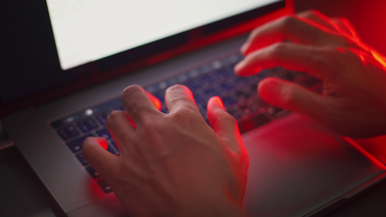 近距离观察黑客的手在有红色应急灯的笔记本电脑上编码。视频下载