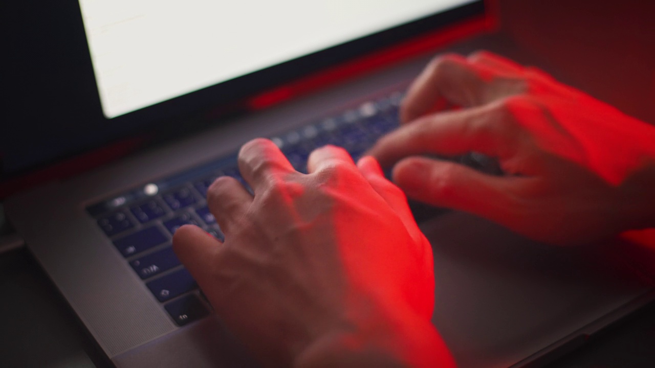 近距离观察黑客的手在有红色应急灯的笔记本电脑上编码。视频下载