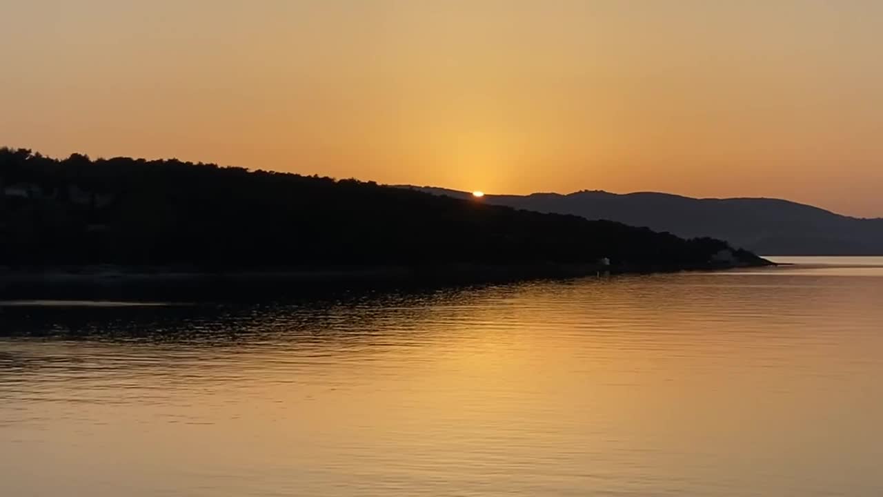 美丽的日落景色在海边与轮廓山和橙色的天空反射放松的水视频素材