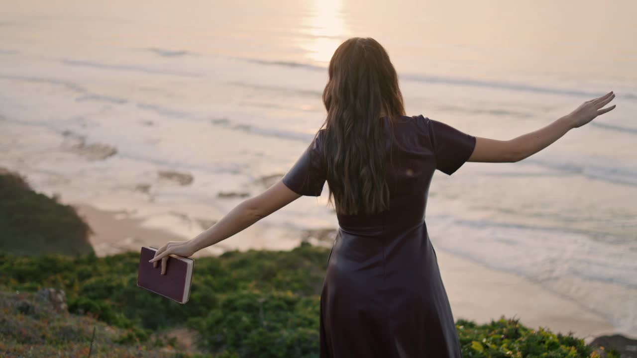 拿着书去海边的女孩。后视图，未知女孩在山上行走视频素材