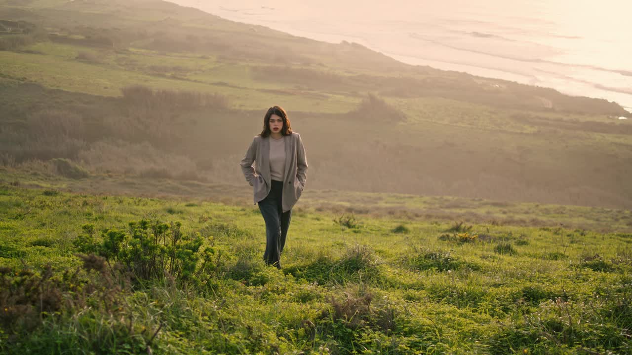 迷人的女孩爬满绿草的小山。女人在平静的海边散步视频素材