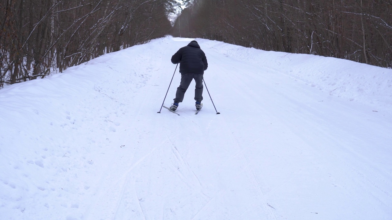 一个50岁的男人冬天在森林里滑雪视频素材