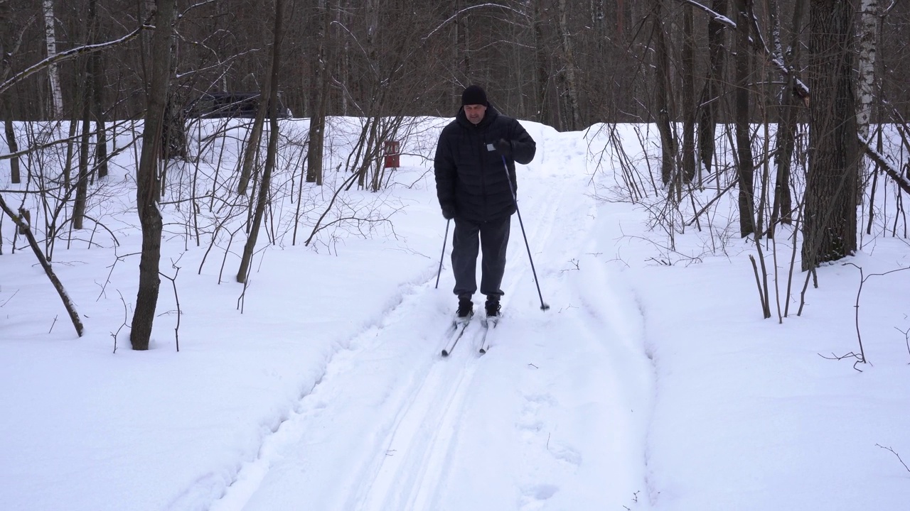 一个50岁的男人冬天在森林里滑雪视频素材