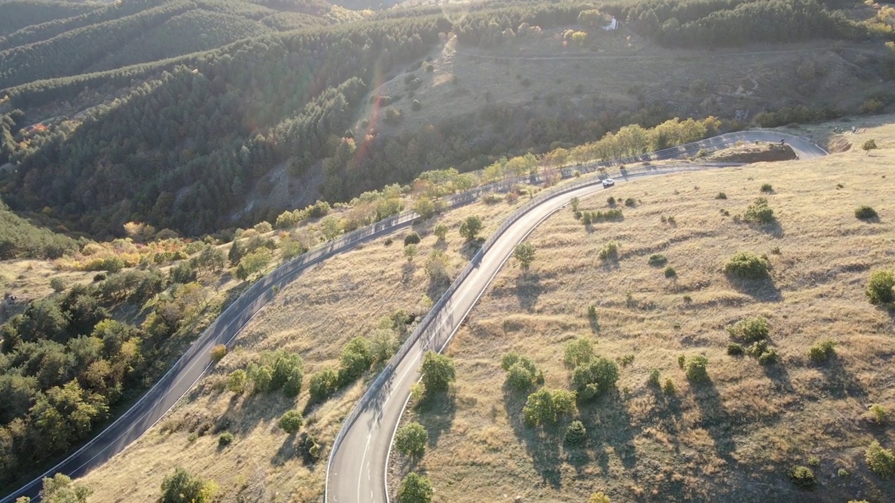 一辆酷酷的定制跑车在日落时加速行驶在风景优美的弯曲山路上的鸟瞰图视频素材