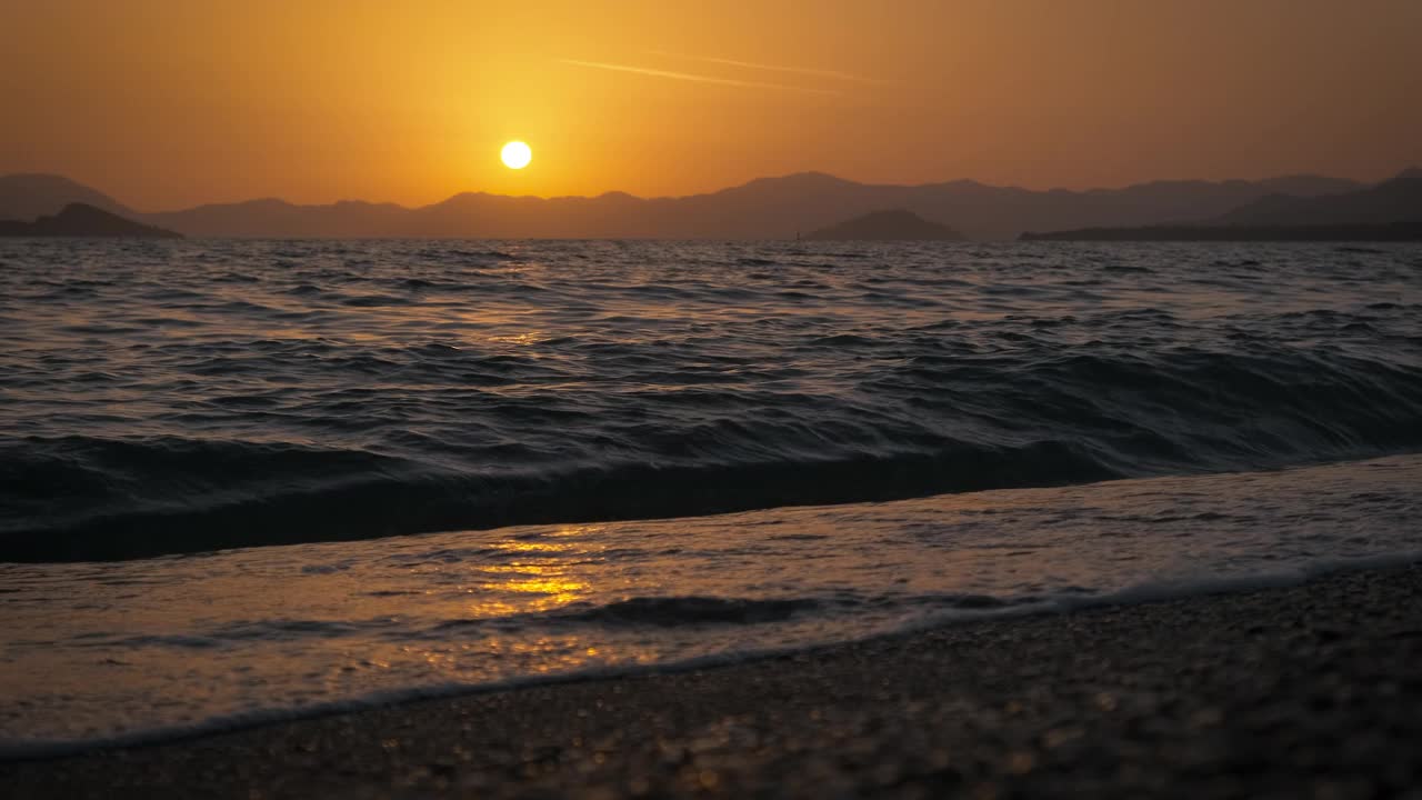 夏日里，五彩斑斓的天空上，橙色的太阳映衬下，空荡荡的泡沫海滩剪影视频素材