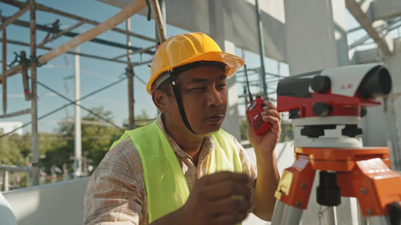 非常集中的亚洲成年土木工程师在一个建筑工地使用经纬仪与复制空间测量视频素材