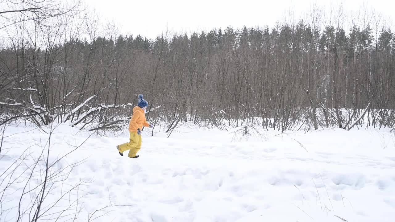 一个穿着黄色衣服的男孩在下雪的公园里沿着小路奔跑视频素材