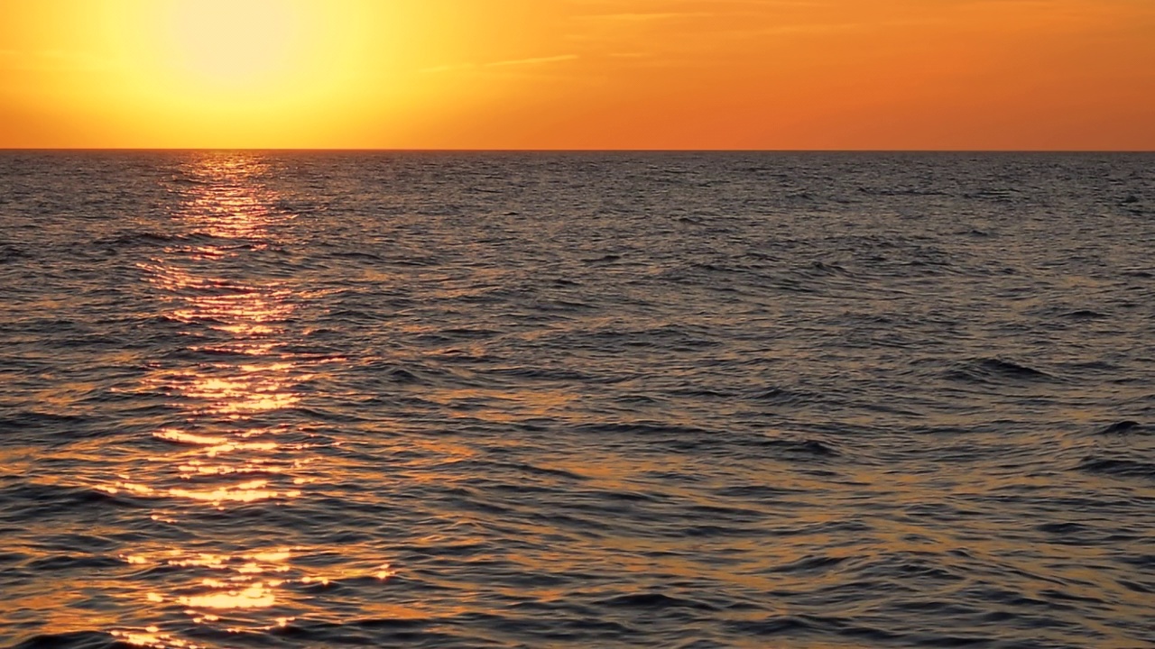 海浪反射黄色和金色的阳光在橙色日落的背景。美丽的阳光与橙色发光的天空，平静的地平线场景在阳光明媚的海滩，中景，慢动作，高清。ProRes 422 HQ。视频素材