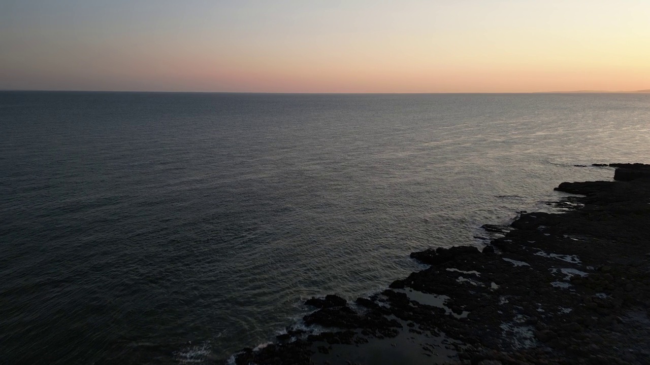 日落时平静的海浪拍打着岩石海岸的航拍照片视频素材