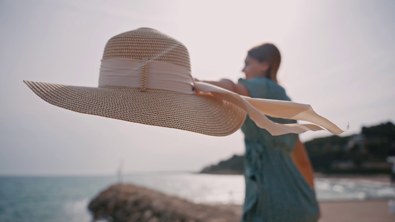 在阳光明媚的夏日，无忧无虑的女人在海滩上拿着太阳帽享受风视频素材