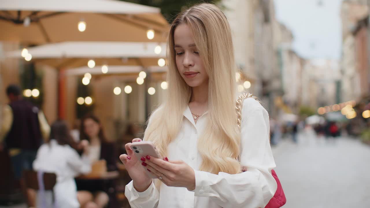 在城市街道外，金发女子用手机庆祝喜讯视频素材