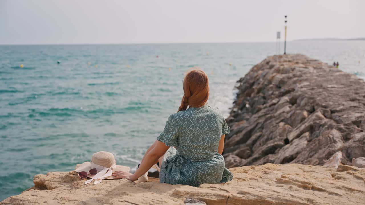 在阳光明媚的夏日，年轻女子在岩石岸边享受海风视频素材