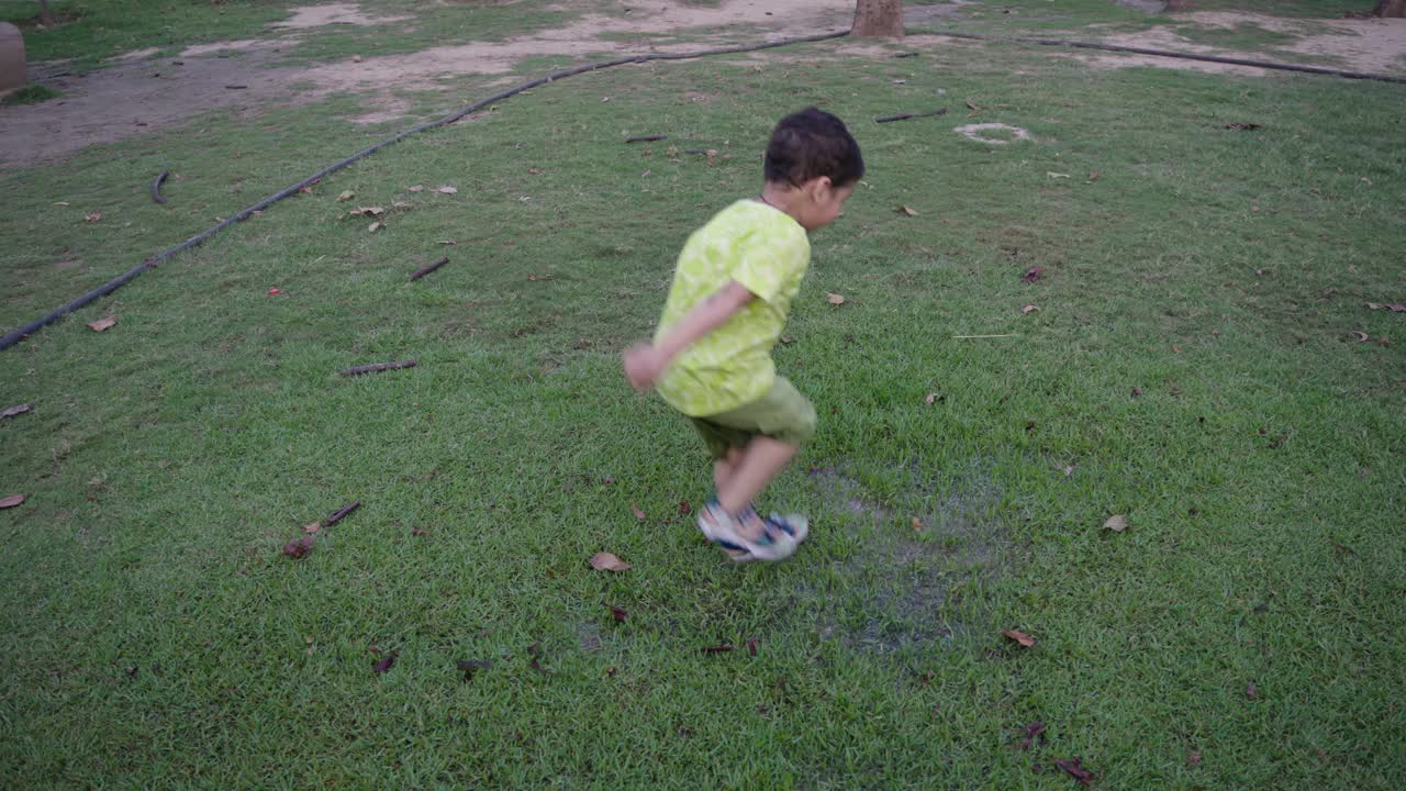 顽皮的男孩在公园草地上的水坑里跳跃视频素材