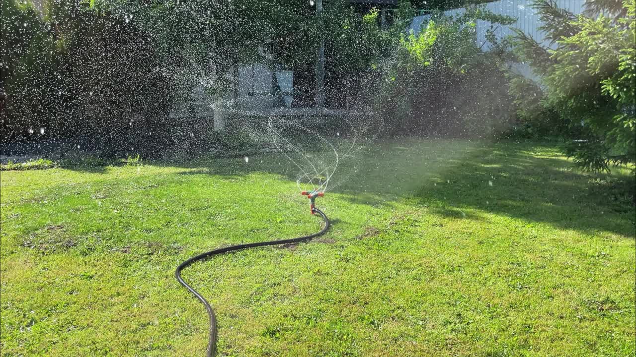 院子里的草坪用喷水器自动浇水。水花在草地上飞舞。户外4k镜头，慢动作视频素材