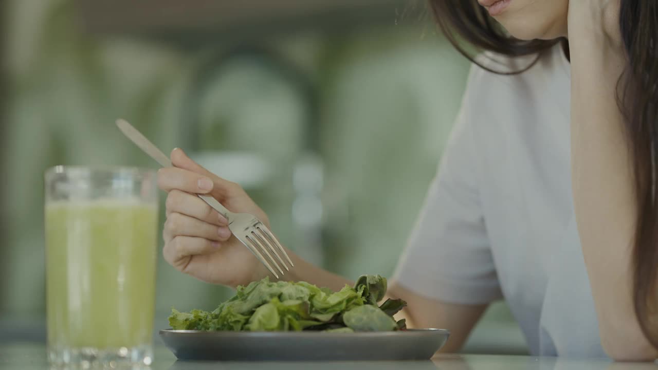 悲伤的女孩试着吃沙拉和健康食品的特写。女孩不喜欢吃绿色的生菜叶子。慢动作视频素材