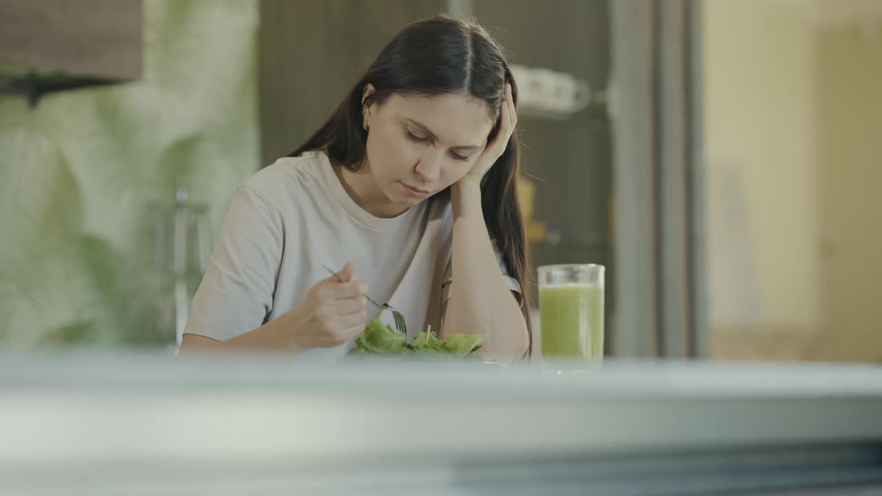 悲伤的节食女孩看着盘子里的生菜叶子，把它们钉在叉子上。特写镜头。慢动作视频下载