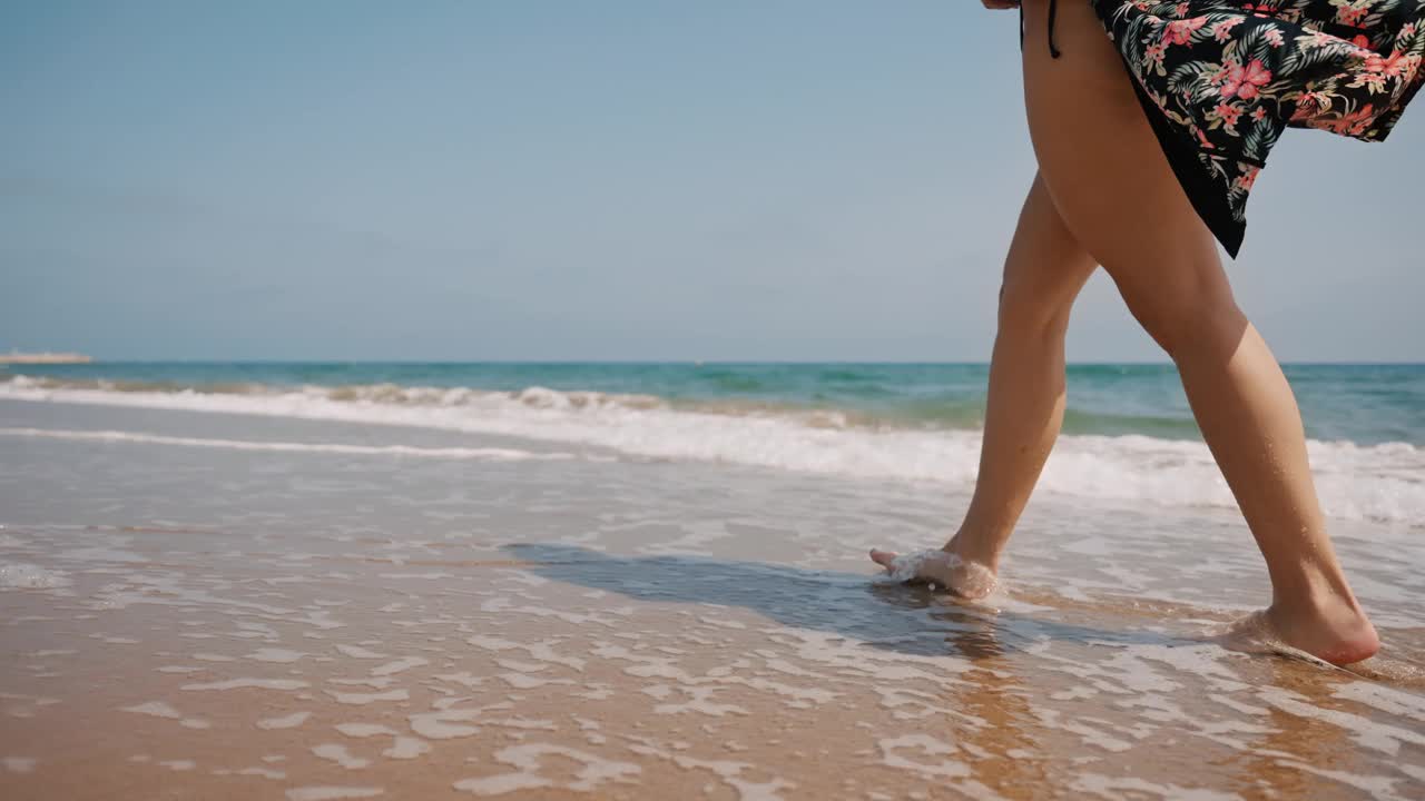 一名女子在沙滩上的海浪中漫步，享受暑假视频素材