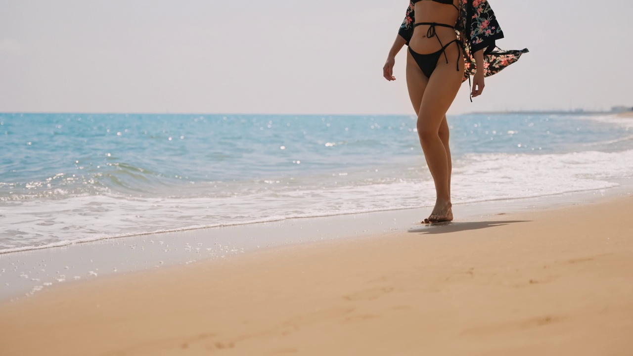 在阳光明媚的夏日里，穿着泳装的女子沿着海浪散步视频素材