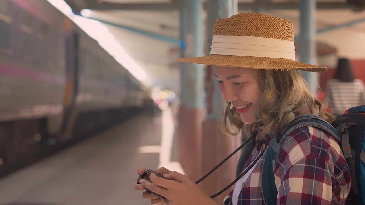 年轻的亚洲女旅客背着背包在铁路上。一名女游客用相机在铁路背景下拍摄火车侧面的照片。积极和旅行的生活方式理念视频素材