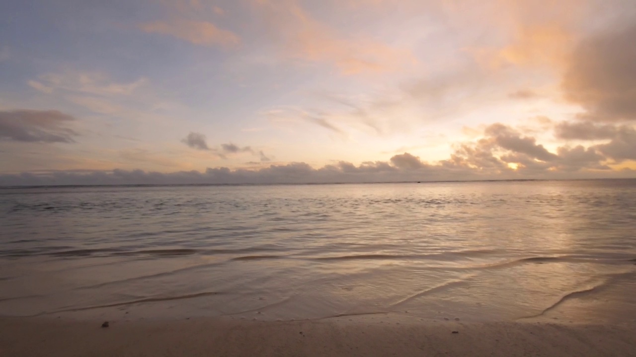 在日落时，太平洋的海洋地平线橙红色的天空与云在平静和放松的绿松石泻湖与柔软的波浪池塘在Aroa拉罗汤加海滩上视频素材