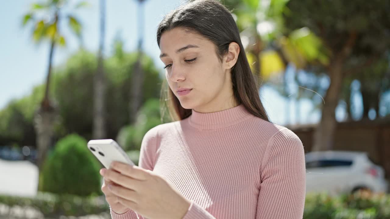 年轻美丽的西班牙女子在公园用智能手机，表情严肃视频素材