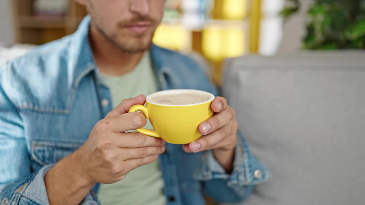 年轻的白人男子坐在家里的沙发上喝咖啡视频素材