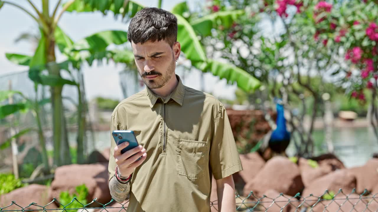 年轻的西班牙男子微笑着自信地在公园用智能手机自拍视频素材