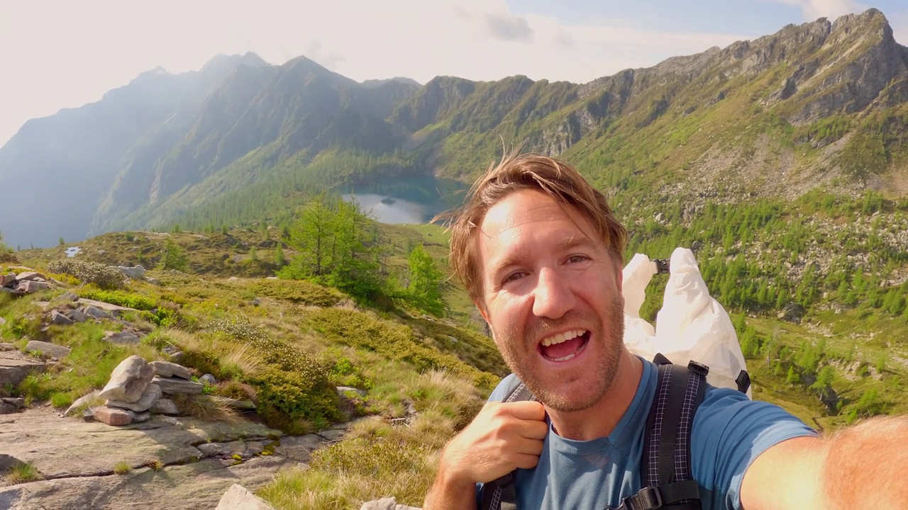 一名男子在群山环绕中徒步旅行，拍了一张很酷的自拍视频素材