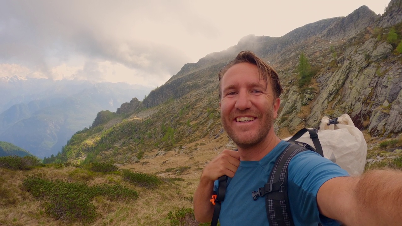 一名男子在群山环绕中徒步旅行，拍了一张很酷的自拍视频素材