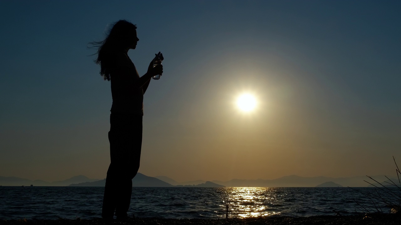 女孩剪影在海湾喝水。视频素材