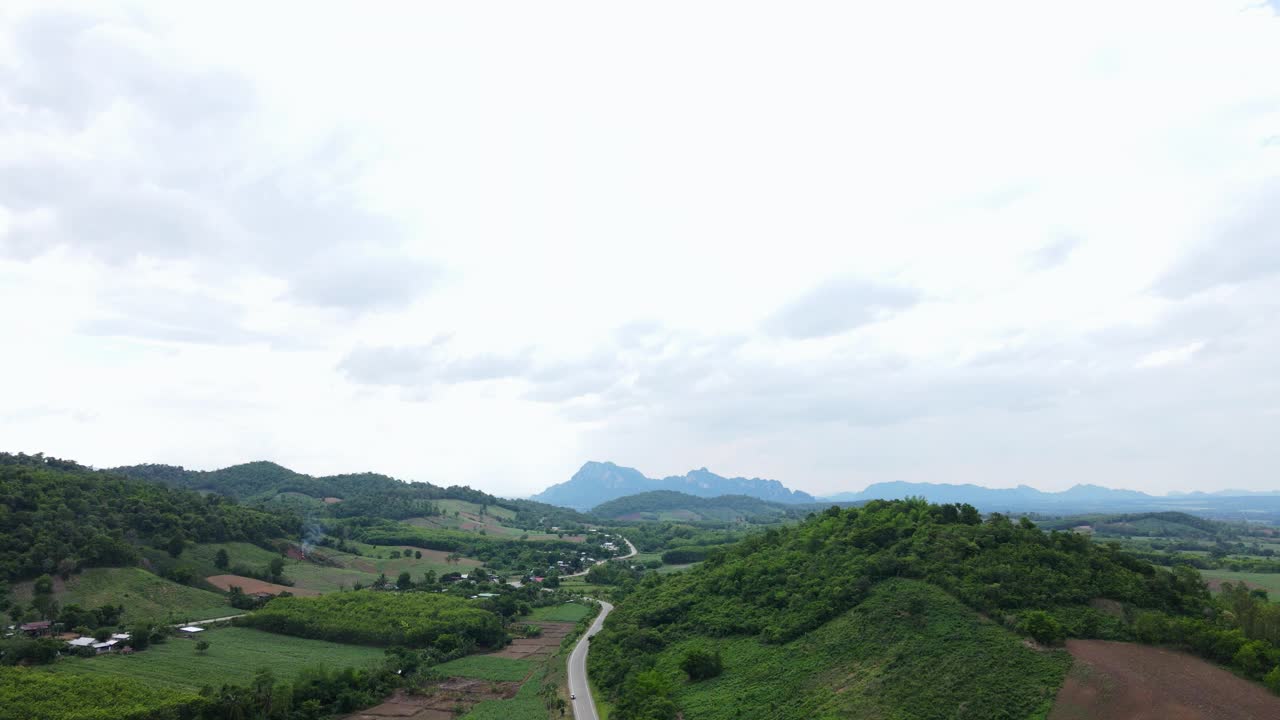 道路穿过郁郁葱葱的大自然，群山环绕着晴朗的天空。视频素材