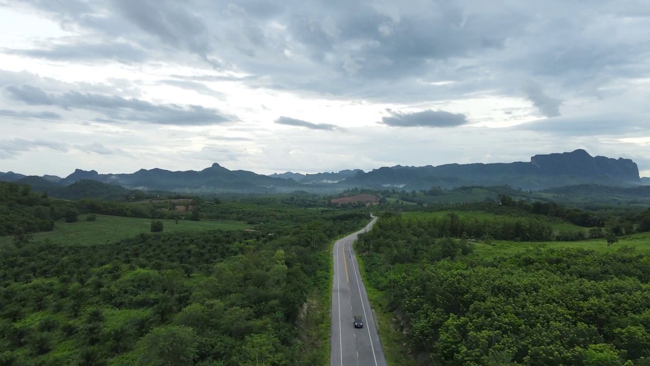 道路穿过郁郁葱葱的大自然，群山环绕着晴朗的天空。视频素材