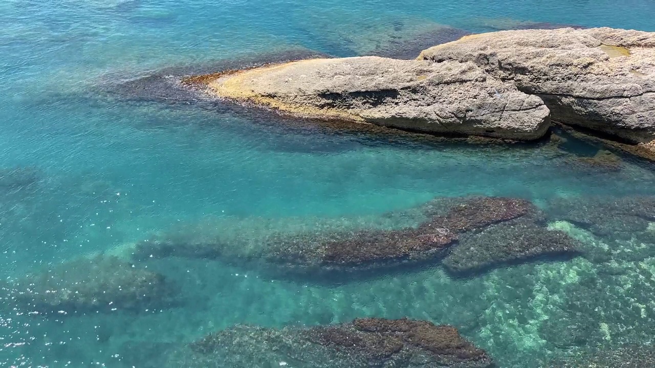 海水蓝蓝的绿松石光泽的表面和岩石海岸鸟瞰。视频素材