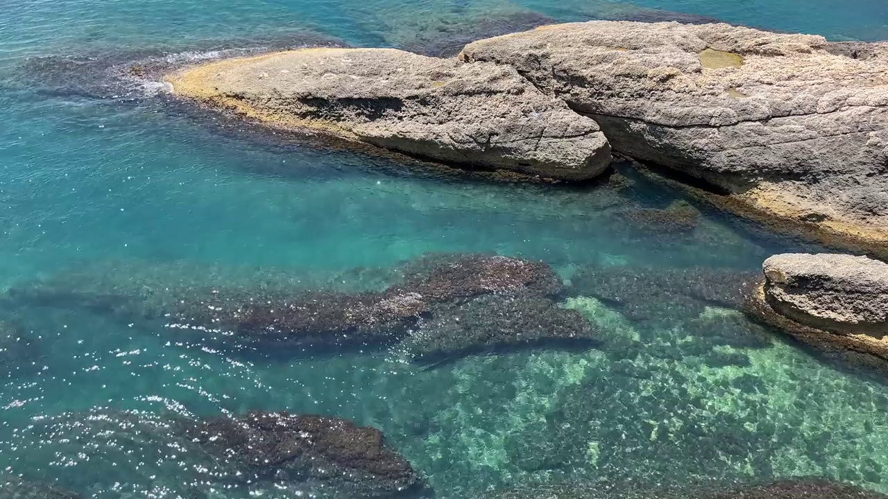 海水蓝蓝的绿松石光泽的表面和岩石海岸鸟瞰。视频素材