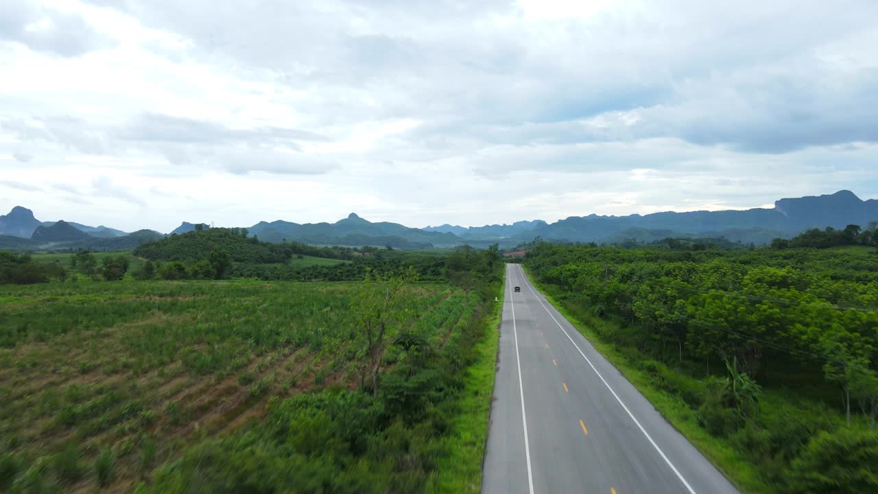 道路穿过郁郁葱葱的大自然，群山环绕着晴朗的天空。视频素材