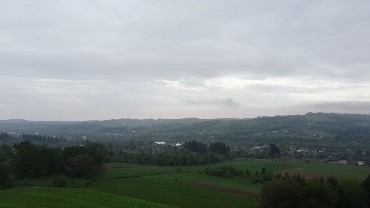 空中无人机拍摄的晨雾在薄雾笼罩的山村上空消散，美丽的大片绿色田野和小房子。乡村景观概念视频素材