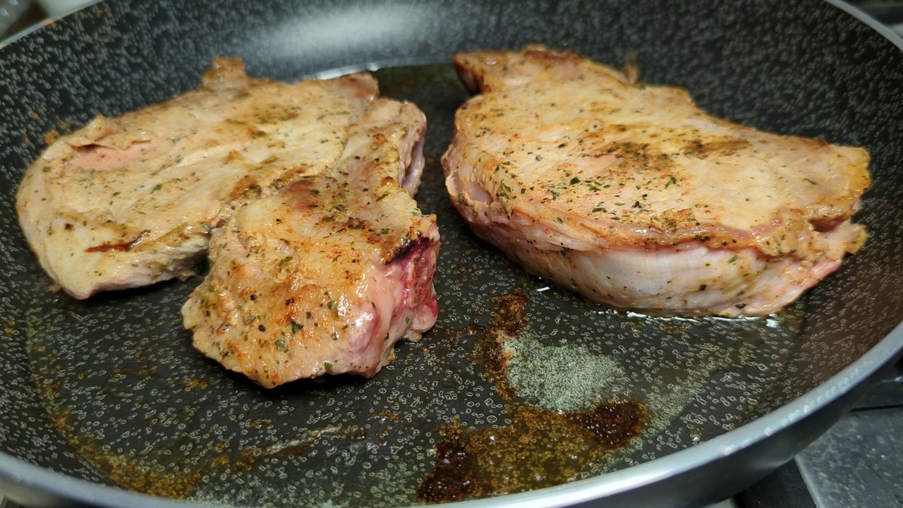 用迷迭香和大蒜调味的美味多汁的猪肉牛排在平底锅里煎。视频素材