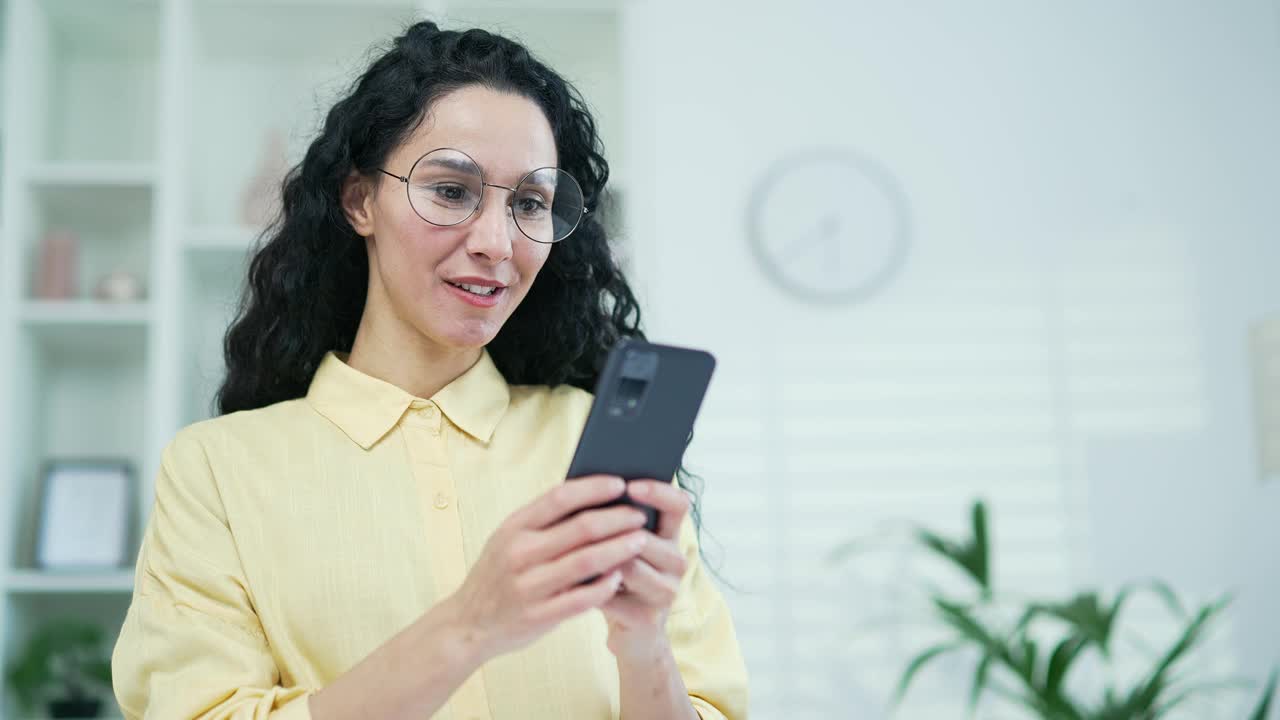 关闭了。快乐的年轻黑发女人在家里的客厅里使用智能手机视频素材