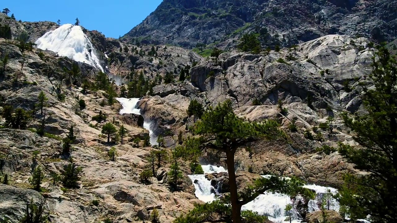 空中拍摄的瀑布在树木中对着山，无人机上升向前在岩石景观-猛犸湖，加利福尼亚视频素材